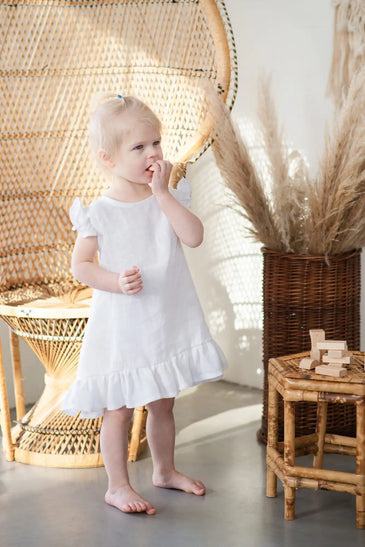 A toddler wears a simple white cotton dress with short flutter sleeves and a ruffled hem.